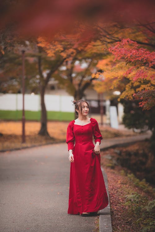 A Woman in Red Long Dress Standing on a Walkway Between Autumn Trees