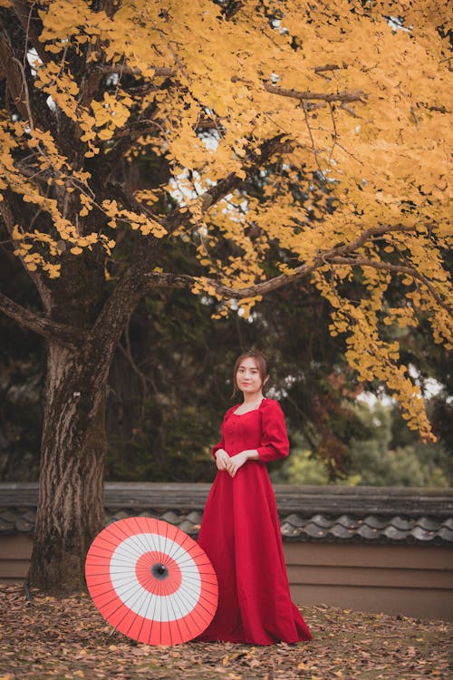 Woman in Red Dress Posing with Umbrella under Tree