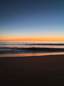 Beautiful sunset at Faro beach, Portugal with vibrant colors and calming ocean waves.
