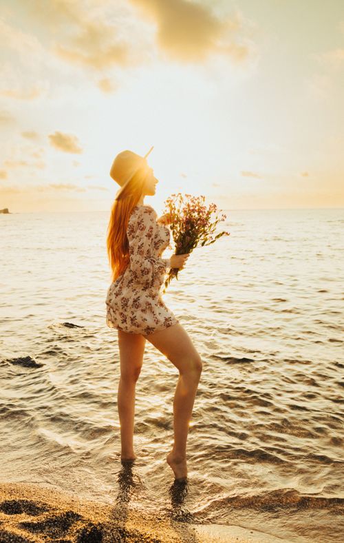 Free Woman in floral dress with bouquet on Turkish beach at sunset. Stock Photo