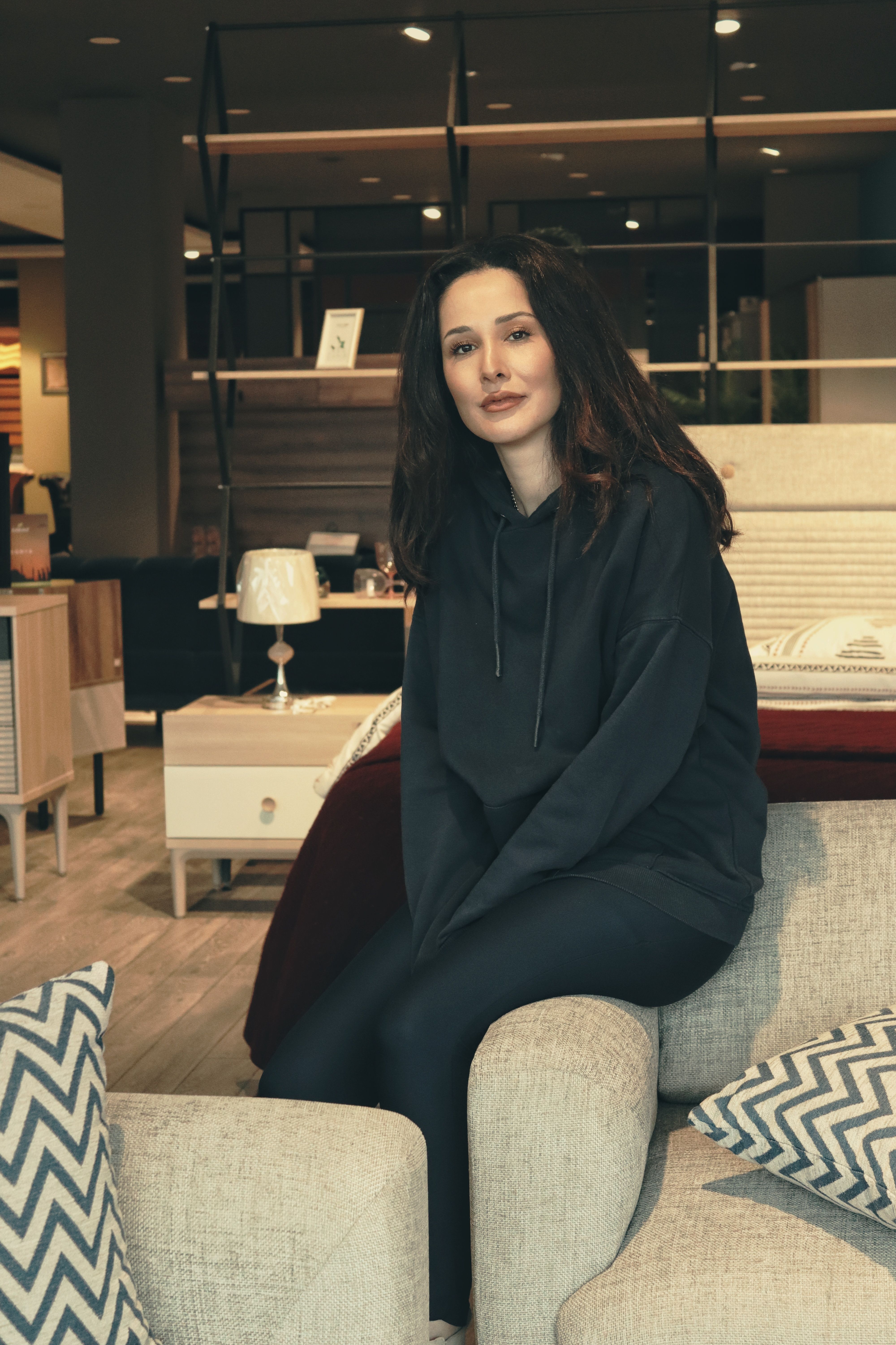 Stylish woman in a hoodie posing in a chic modern living room setting.