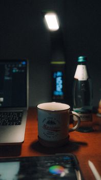 Warm desk scene with ceramic mug, laptop, and water bottle under soft light.