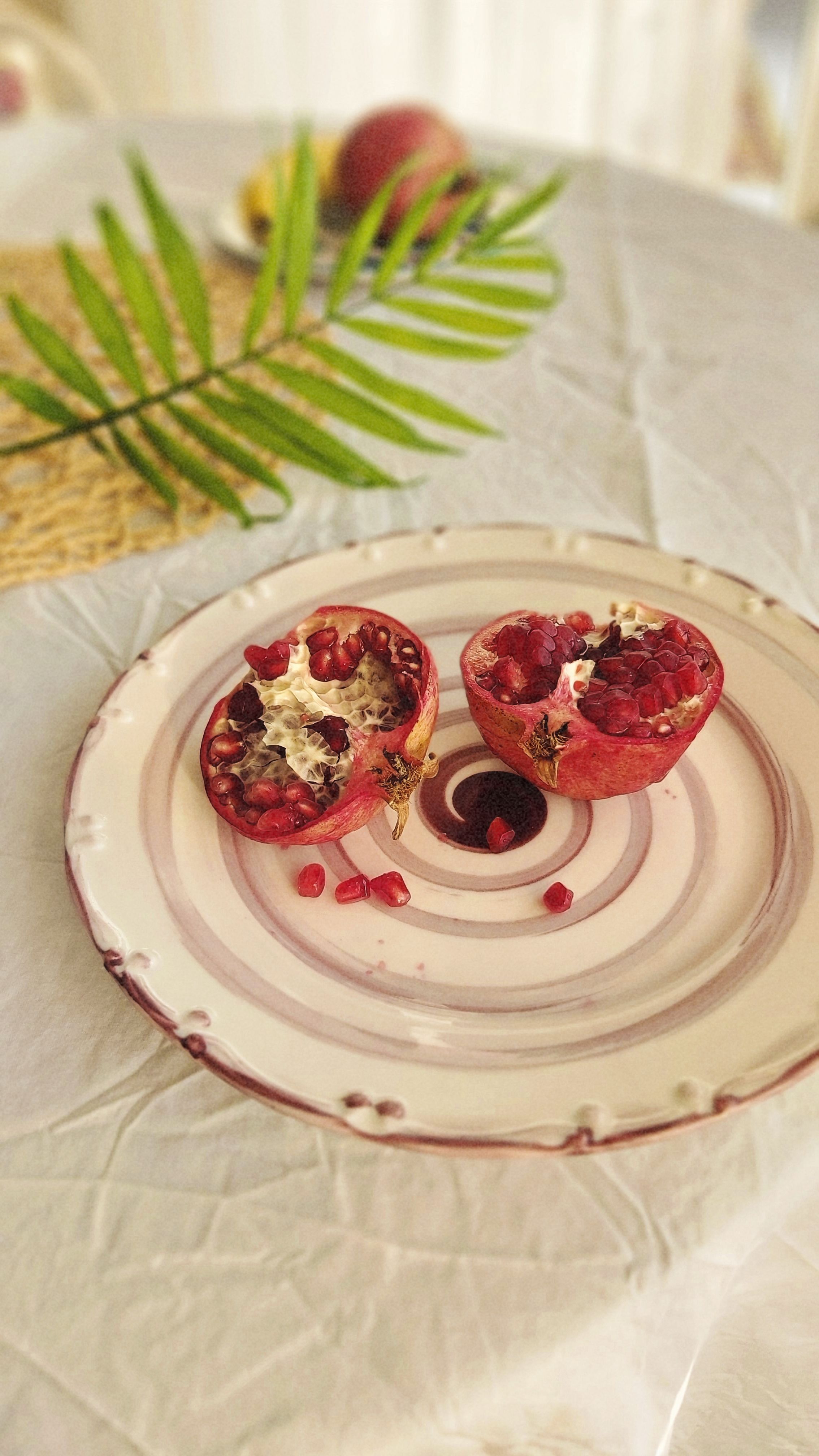 A beautifully arranged still life featuring a sliced pomegranate on a ceramic plate with green leaves.