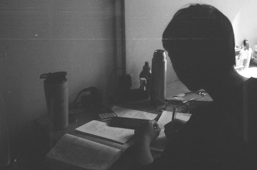 Free A man writes in a notebook with a pen in a monochrome indoor setting. Stock Photo