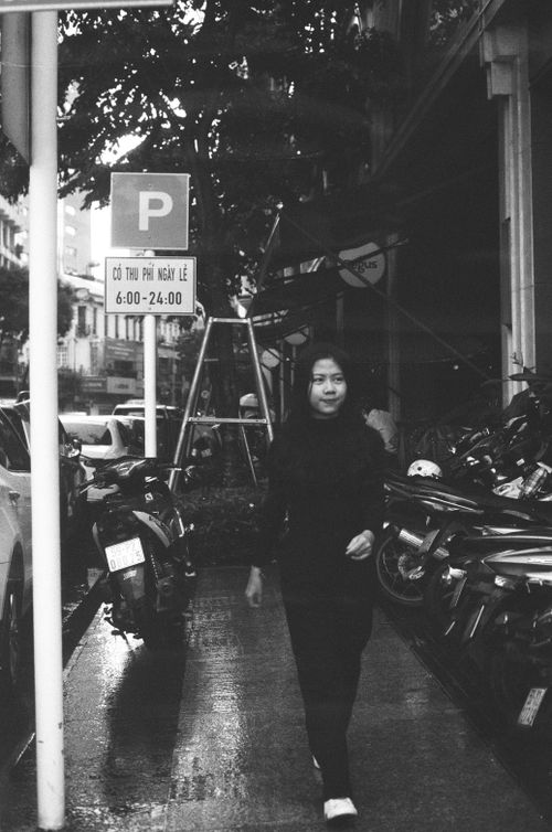Free Black and white photo of a woman walking on a city sidewalk, surrounded by parked motorcycles. Stock Photo