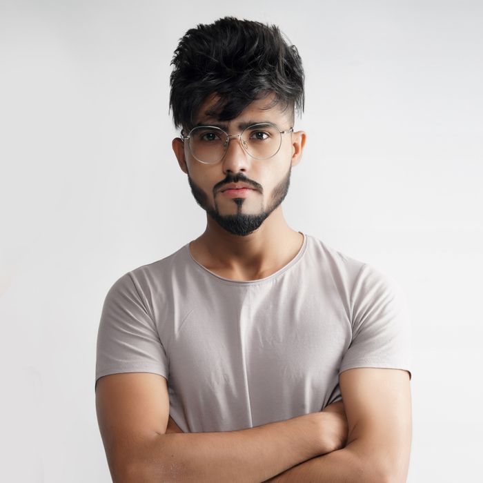 Man wearing a plain stone-coloured short-sleeve top against a pale studio wall — photo by addy bronzzz on Pexels