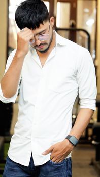 Portrait of a man in a white shirt with eyeglasses, posing thoughtfully indoors.