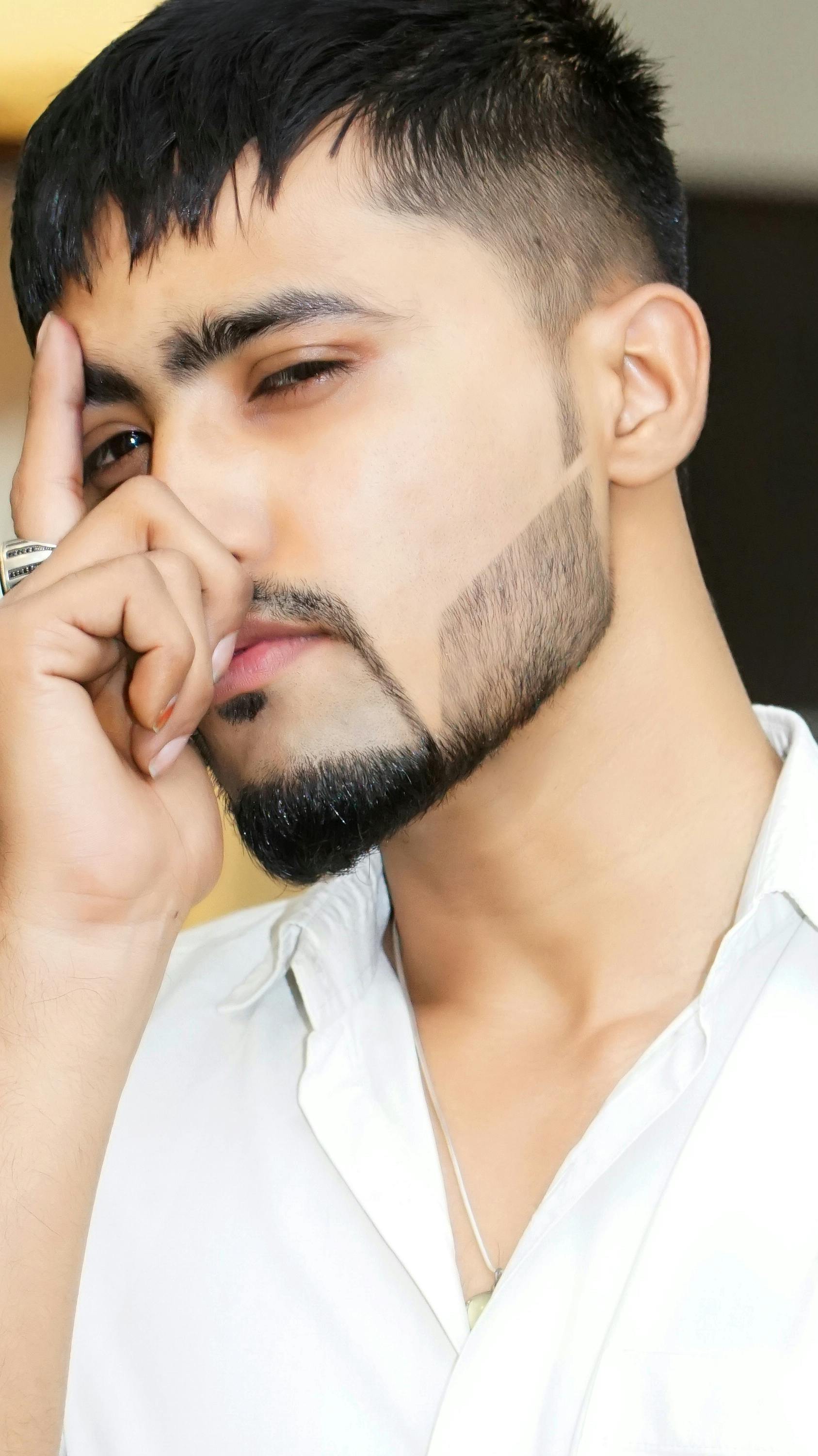 Close-up portrait of a stylish young man with a groomed beard and contemplative pose indoors.