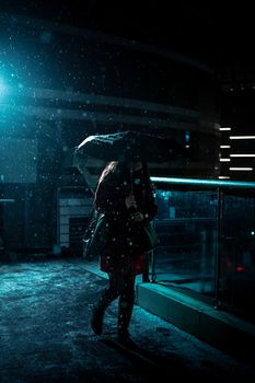 A woman walks with an umbrella during a snowy night in an urban environment.