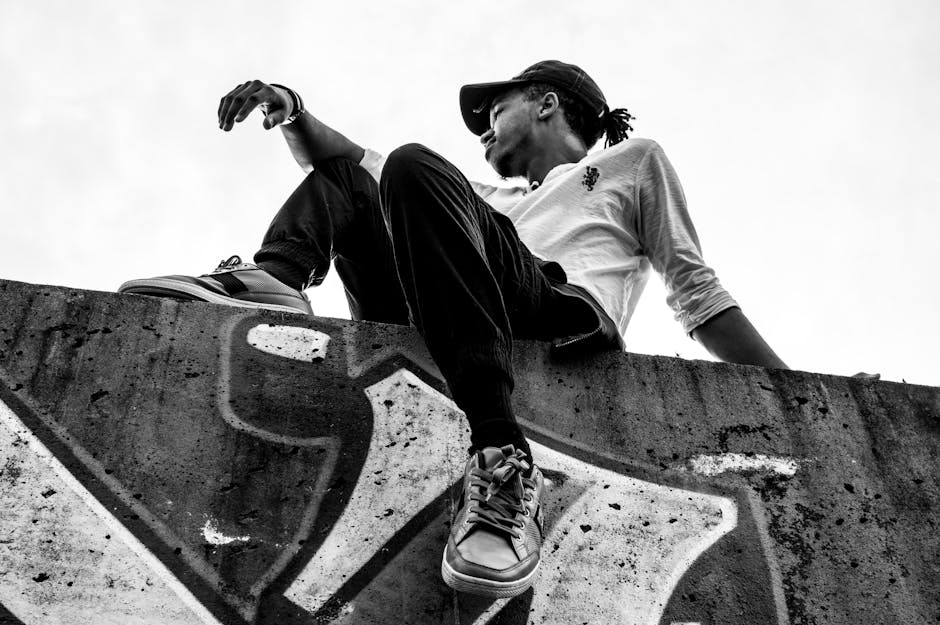 Black and white portrait of a man sitting on a graffiti wall, outdoors