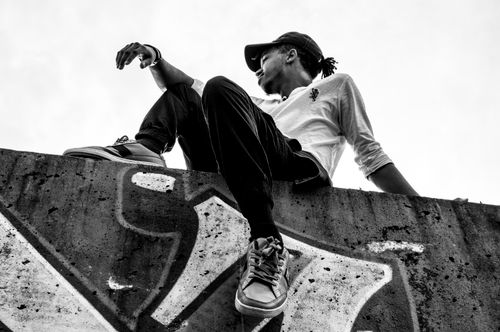Free Black and white portrait of a man sitting on a graffiti wall, outdoors. Stock Photo