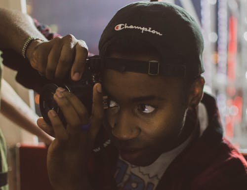 Person Holding Camera Wearing Black Champion Cap