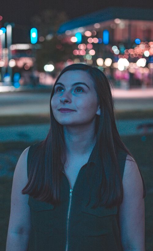 Free Portrait of a young woman gazing upwards amidst urban night lights. Stock Photo