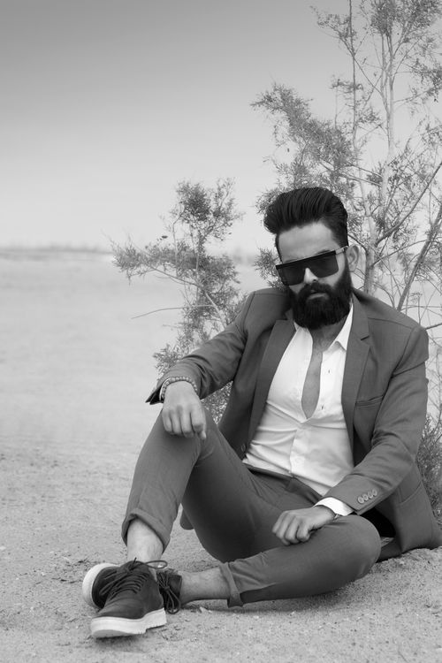 Free Black and white portrait of a fashionable man sitting in a desert setting wearing sunglasses. Stock Photo