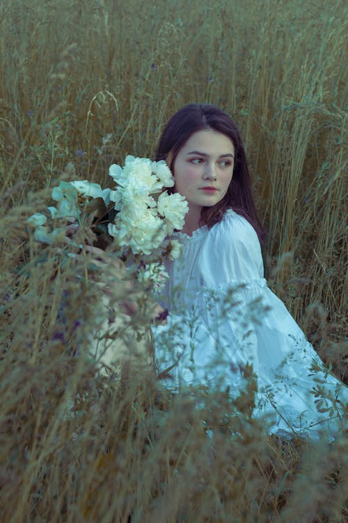 Woman in White Dress Holding Flowers on Grass Field 