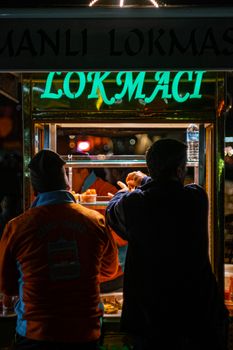 Men selling traditional street food at night in a bustling market.