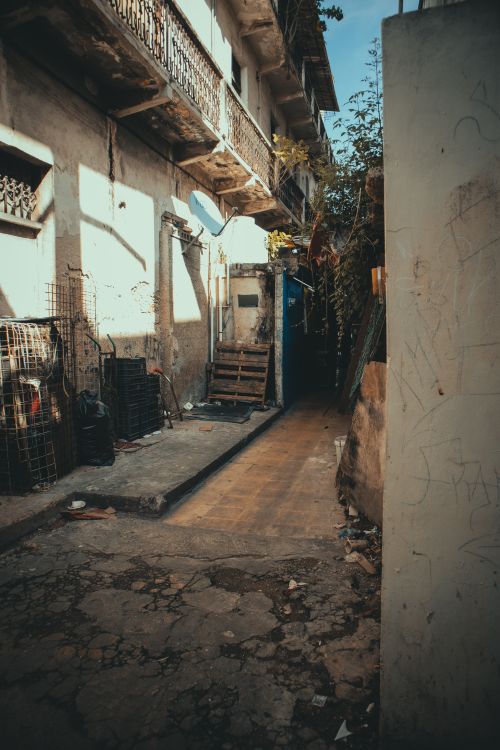 Free Atmospheric view of a narrow urban alley with old, weathered buildings and sunlight casting shadows. Stock Photo