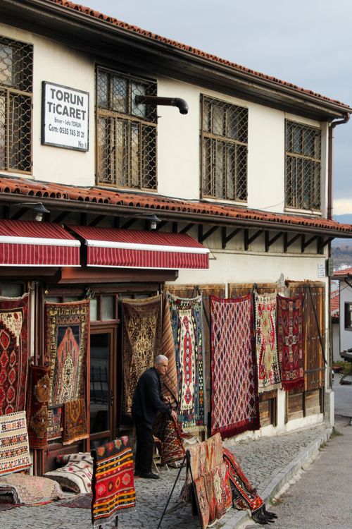 Free Elderly man adjusting rugs outside a traditional carpet store in Ankara, showcasing Turkish craftsmanship. Stock Photo