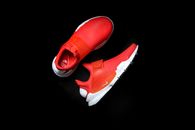 Top view of modern pair of sneakers with red texture and rubber inserts holding right form comfortable for foot and white soles placed on black glance surface