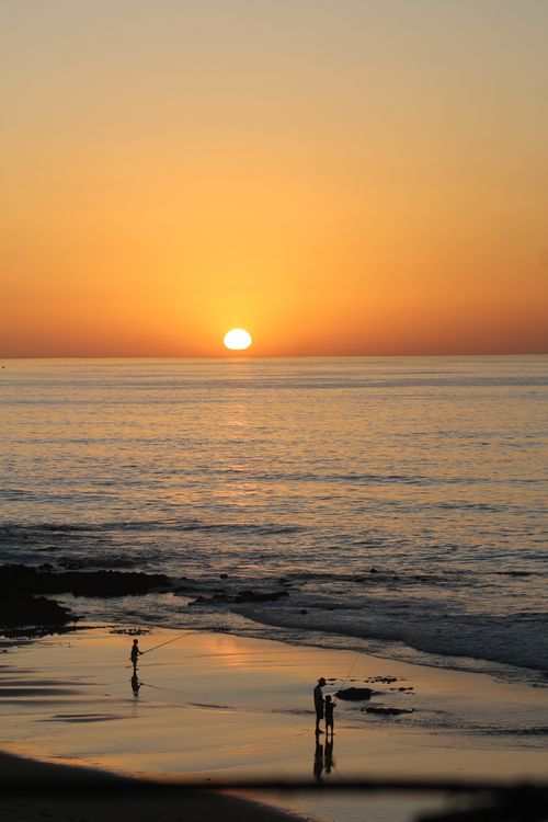 Free Tranquil sunset over ocean with silhouettes on a sandy beach in Marrakesh, Morocco. Stock Photo