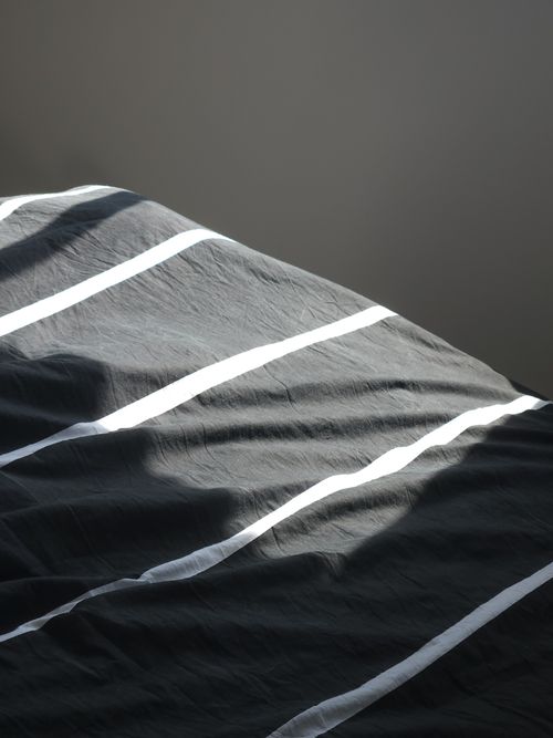 Free A close-up of a crumpled bed sheet with striped patterns under natural sunlight. Stock Photo