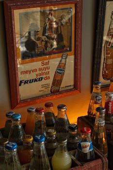 Collection of vintage glass soda bottles with retro advertising posters in the background.