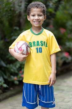 Cheerful boy in Brazil jersey holding a soccer ball, smiling outdoors.