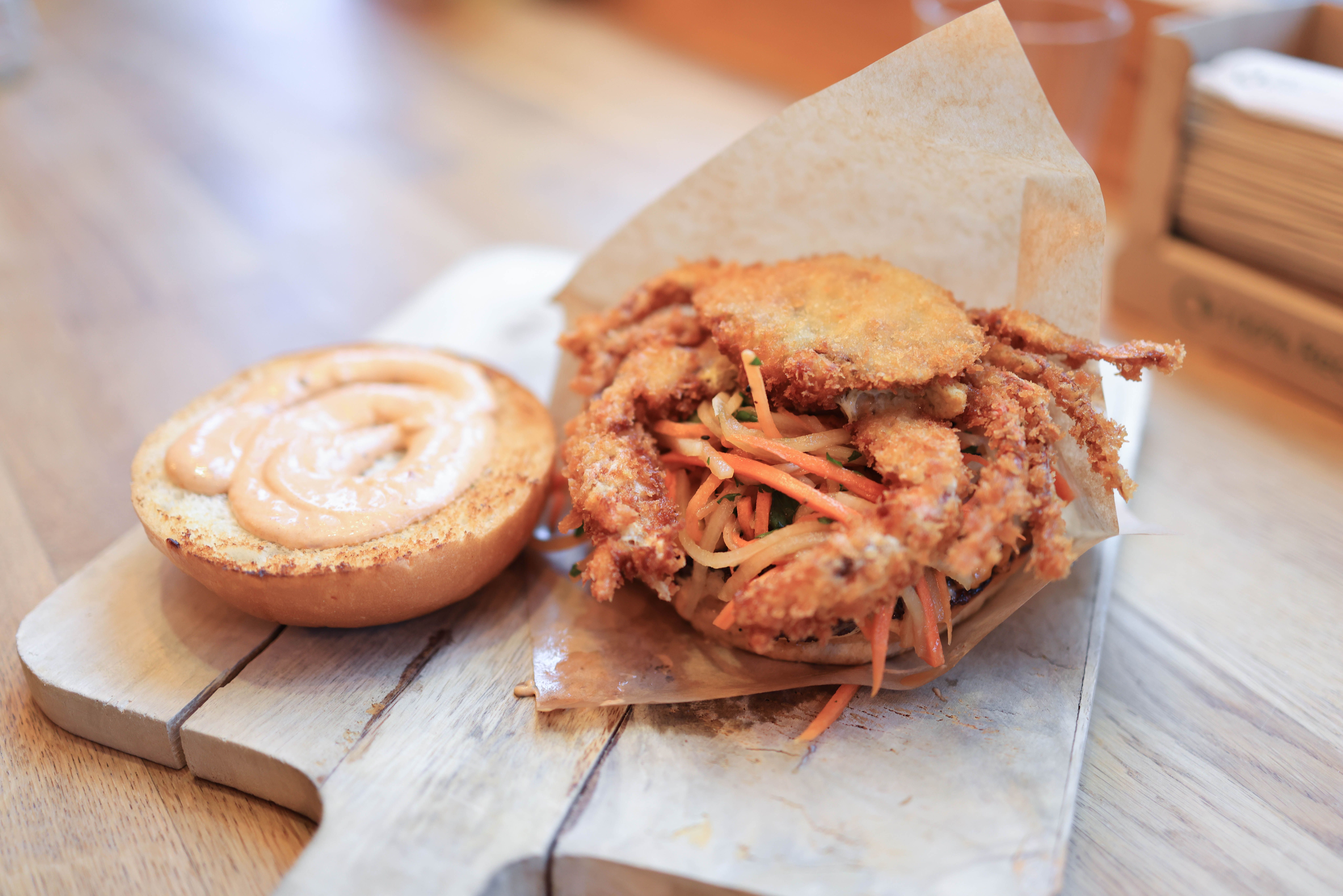 Mouth-watering soft-shell crab sandwich with spicy mayo and slaw on a wooden board.