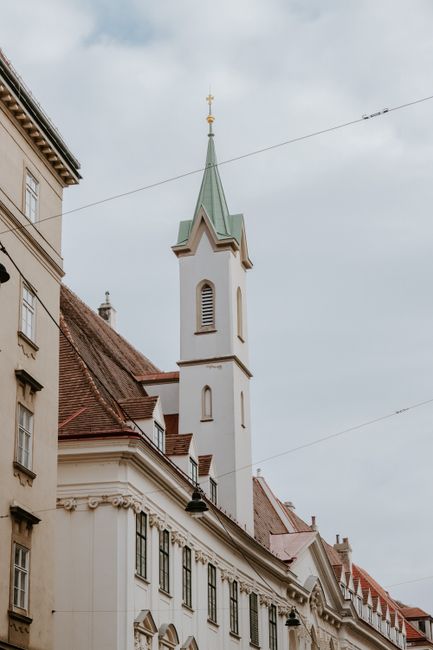 Low-angle shot of a historic Gothic-style church tower in Vienna's urban landscape.