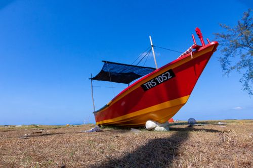 Free Colorful fishing boat resting on dry grass by the sea under blue skies. Stock Photo