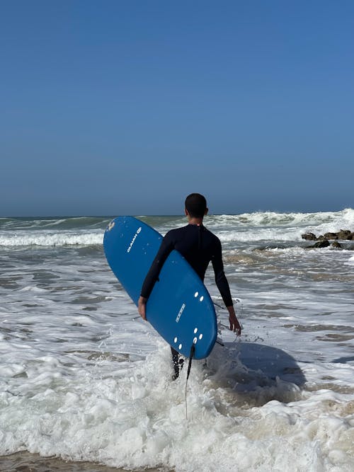 Man Carrying His Surfboard Walking on Seashore