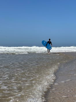 A solo surfer walking towards the ocean with a surfboard, ready to catch waves.