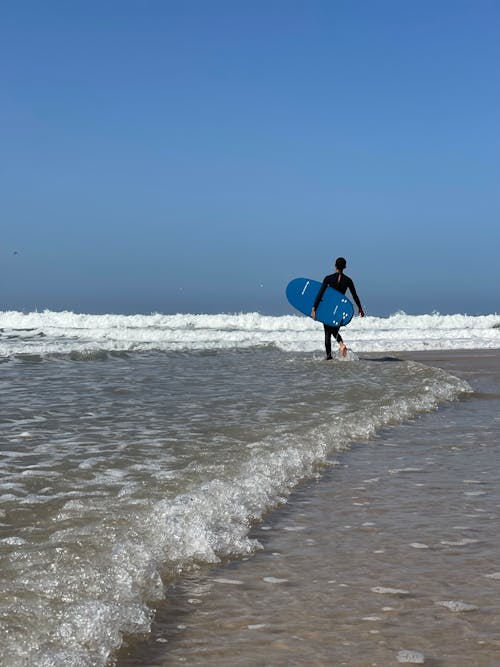 Free Surfer on Seashore Carrying a Surfboard Stock Photo