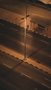A quiet city street at night illuminated by a lone street light, with an empty waiting shed in view.