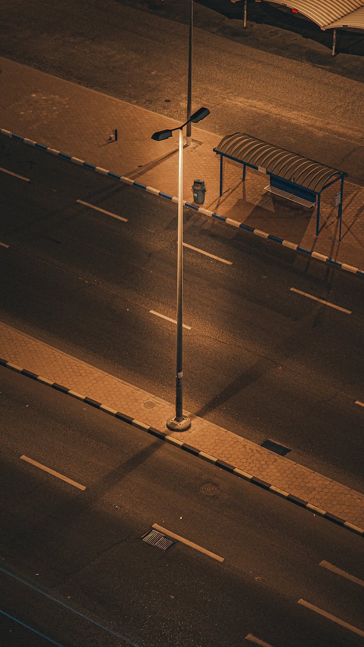 An Aerial Photography Of An Empty Road With Metal Post And Waiting Shed On The Street At Night