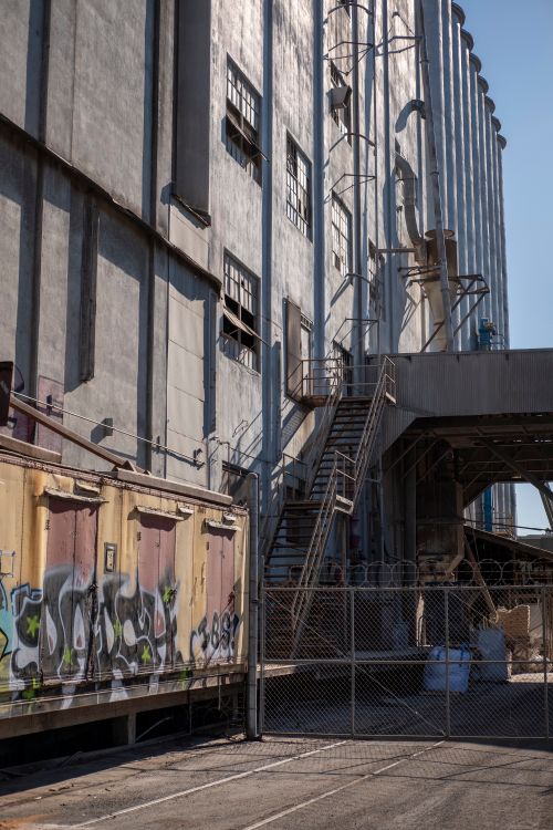 Free Urban industrial scene featuring a graffiti-covered wall and metal stairs set against an industrial building facade. Stock Photo