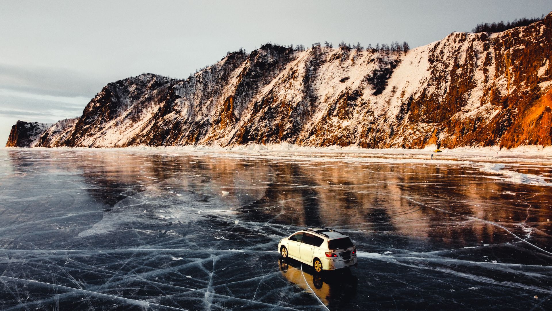 A white Toyota SUV parked on the frozen surface of Lake Baikal against a backdrop of snow-covered cliffs during winter.