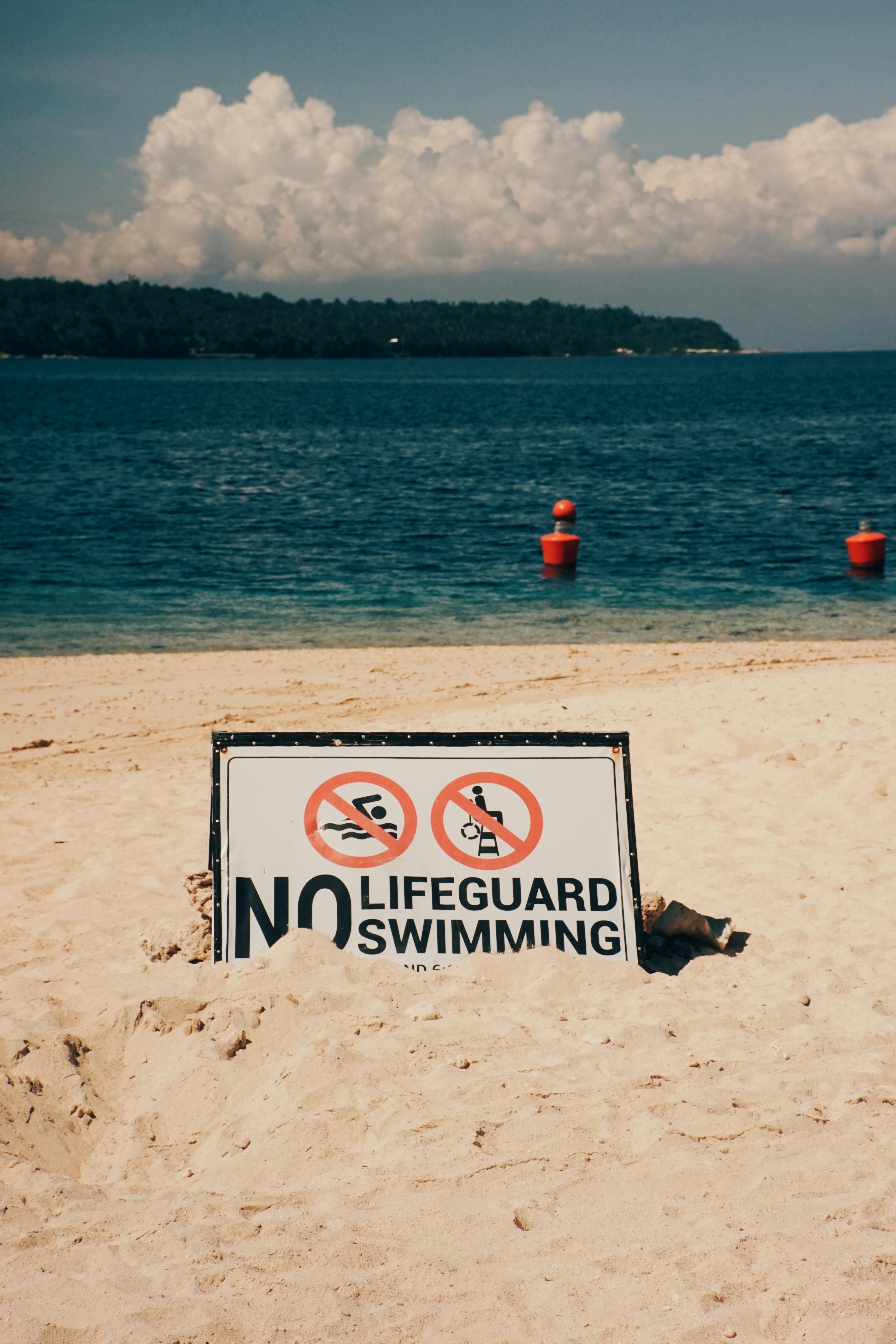Beachside warning sign indicating no lifeguard and no swimming allowed, set against a tranquil ocean backdrop.