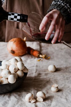 A cozy kitchen setup featuring wine pouring, mushrooms, and vegetables for a rustic meal.