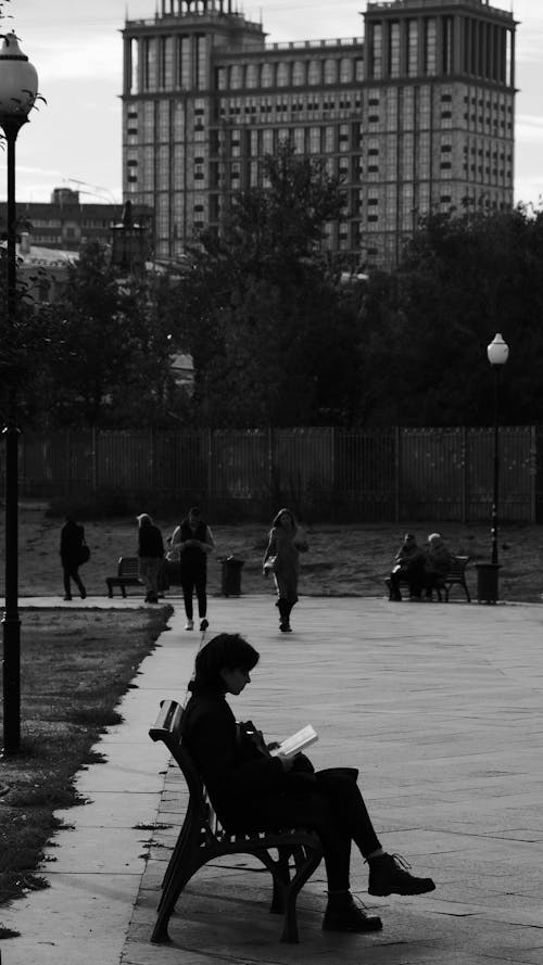 Grayscale Photo of Woman Sitting on Bench While Reading a Book