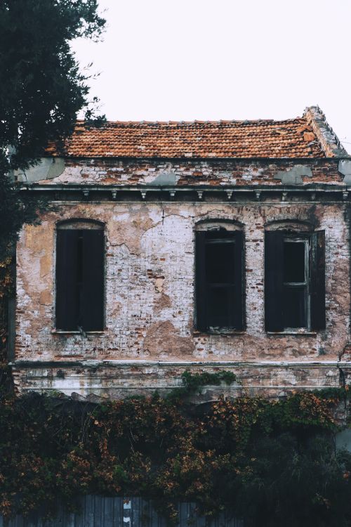 Free A damaged and abandoned brick building with overgrown bushes, showcasing decay and urban exploration. Stock Photo