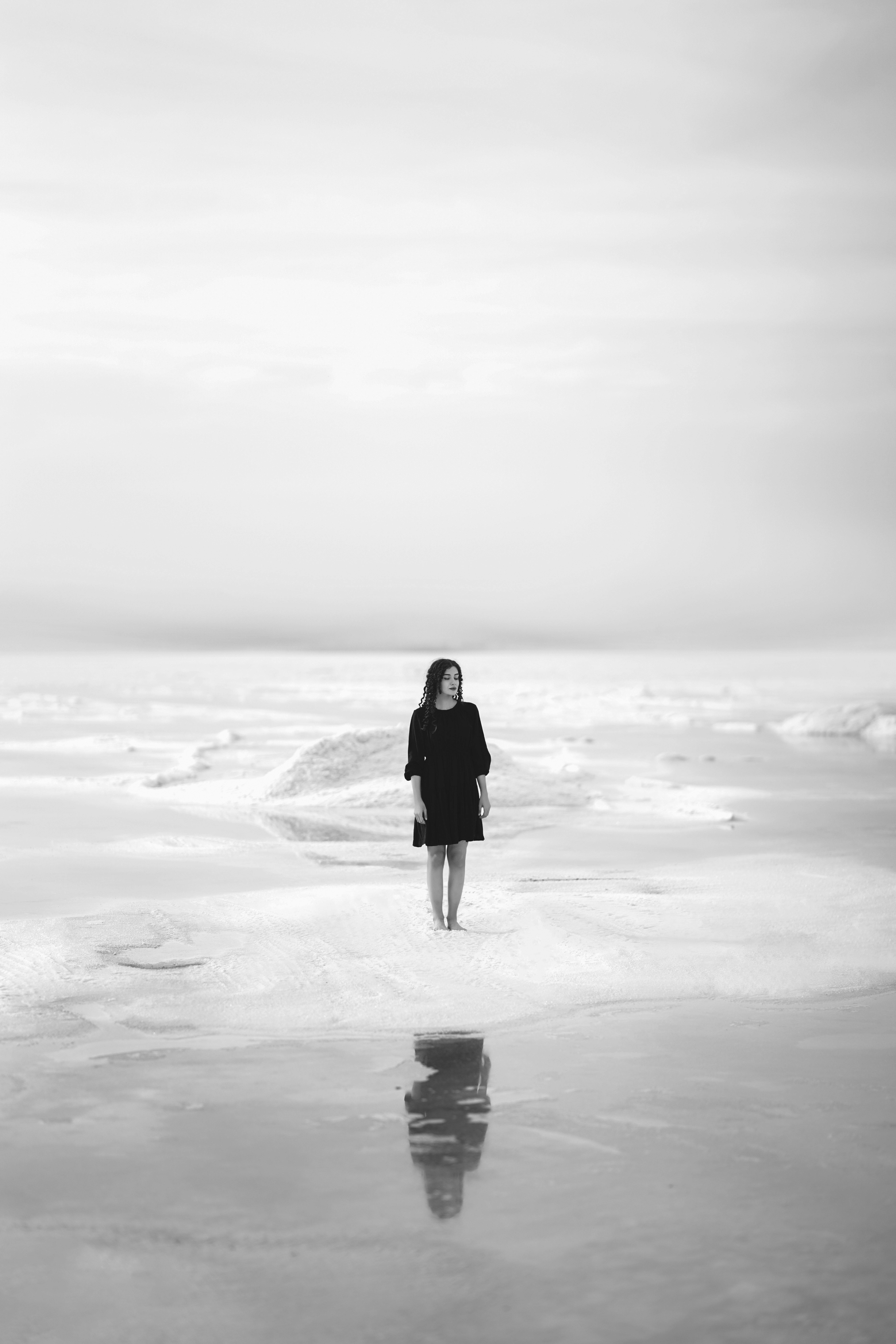 Black and white photo of a woman in solitude on the beach, creating a reflective mood.