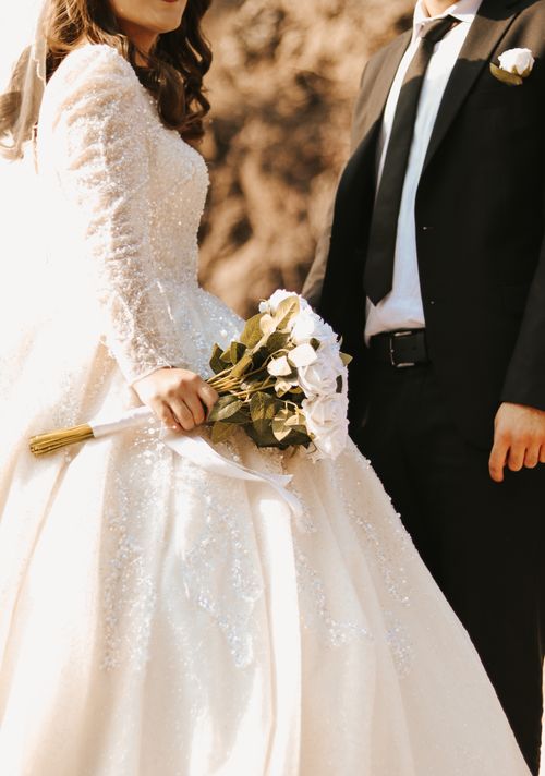 Free Close-up of bride and groom holding white rose bouquet in wedding attire, showcasing elegance. Stock Photo