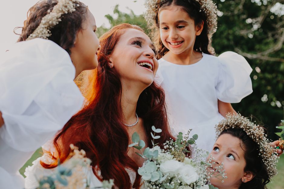 A happy family gathering of a woman and three young girls wearing flower headbands and white dresses outdoors.