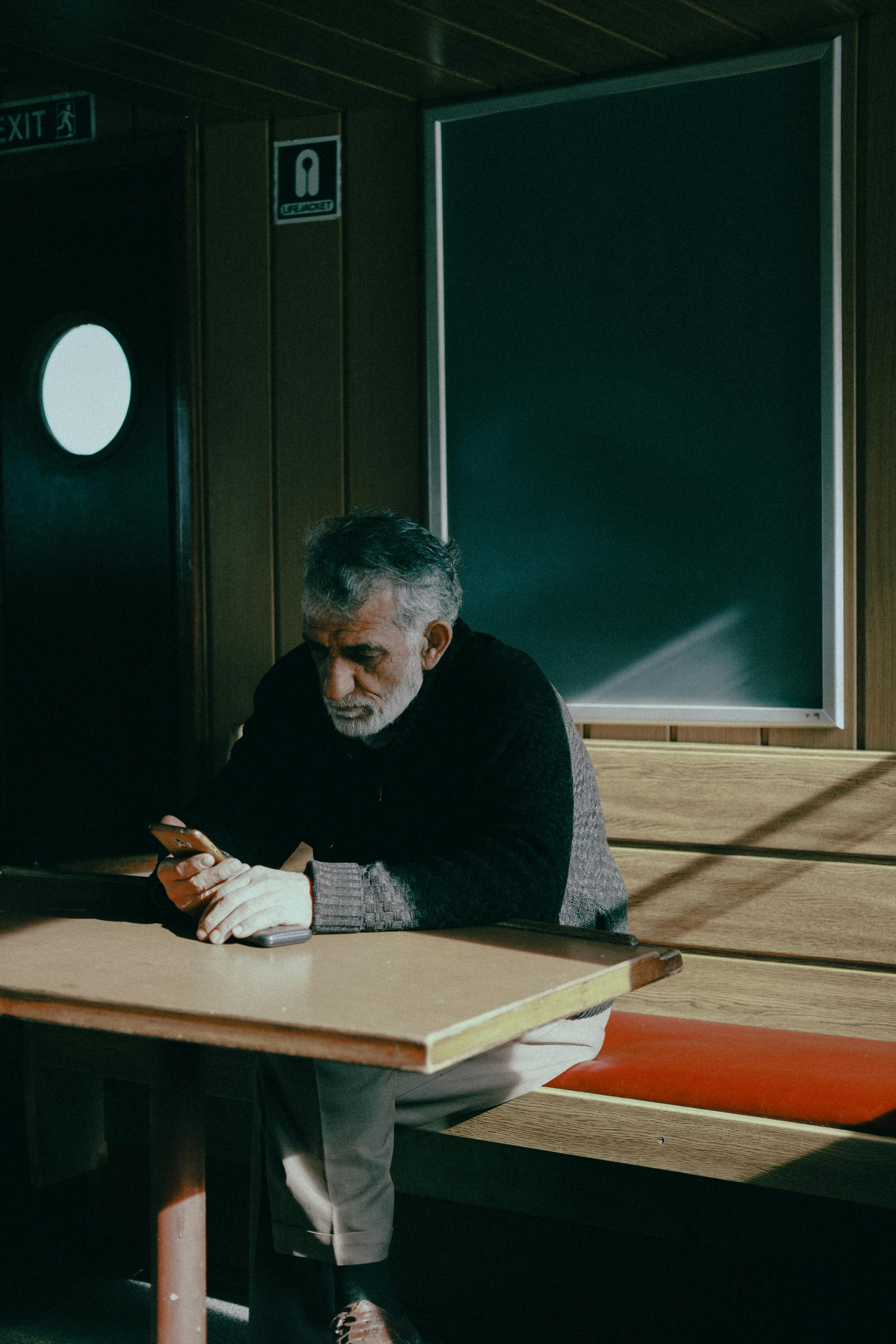 man sitting on a bench by a table and using his phone