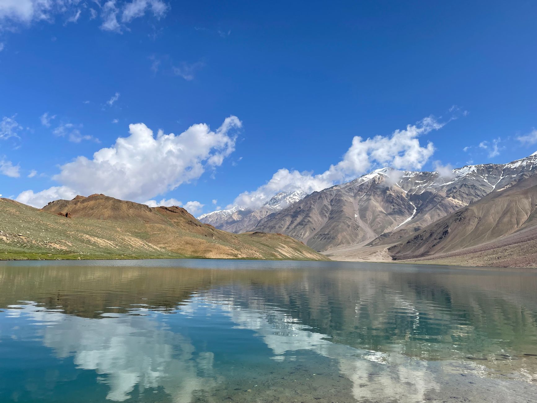 A breathtaking view of a mountain lake reflecting snowy peaks under a blue sky.