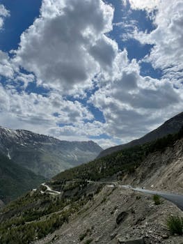 Majestic mountain landscape with a winding road under a dramatic cloudy sky, perfect for nature enthusiasts.