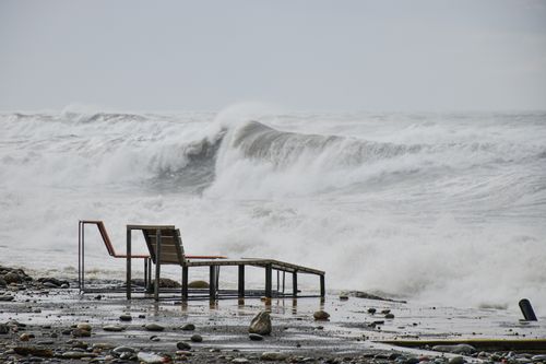 Free A stormy seashore with big waves crashing onto the beach. Empty beach chair frames are visible amidst the turbulent sea. Stock Photo