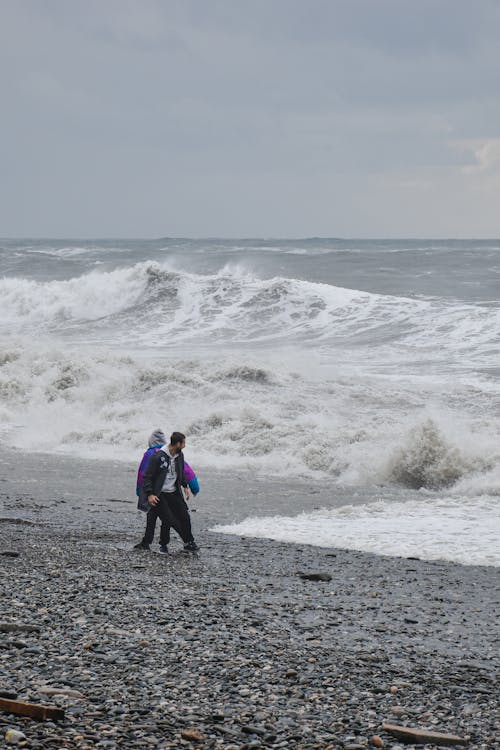 Men on Seashore Looking at Crashing Waves