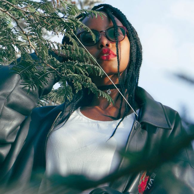 A young woman with sunglasses and leather jacket poses outdoors in Juja, Kenya.